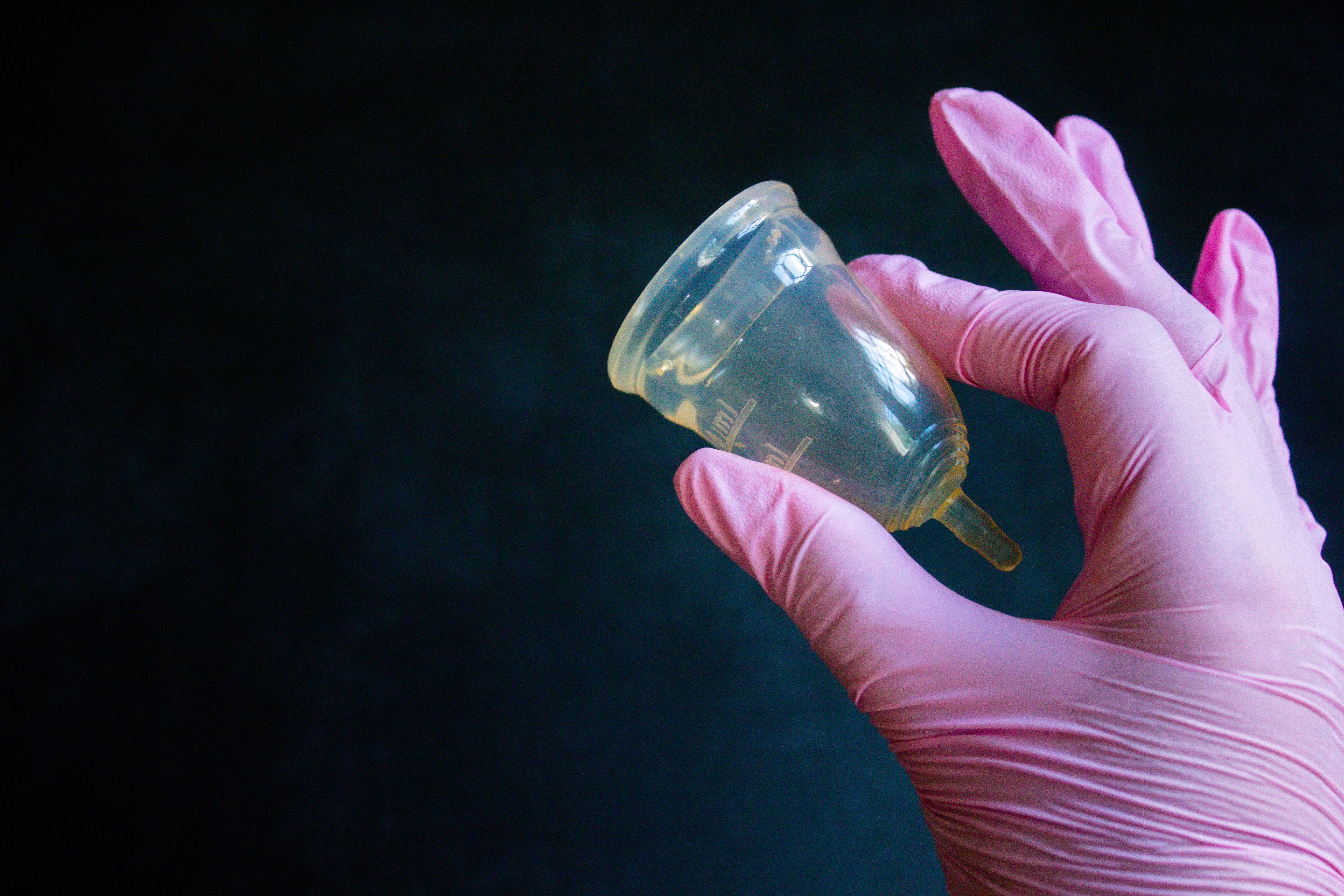A gloved hand holding a menstrual cup against a dark background, promoting eco-friendly hygiene.
