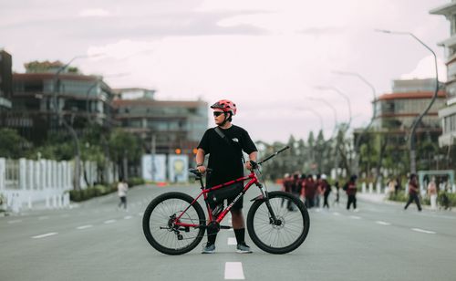 Free Adult man with a mountain bike stands confidently on a city street, wearing a helmet and sunglasses. Stock Photo