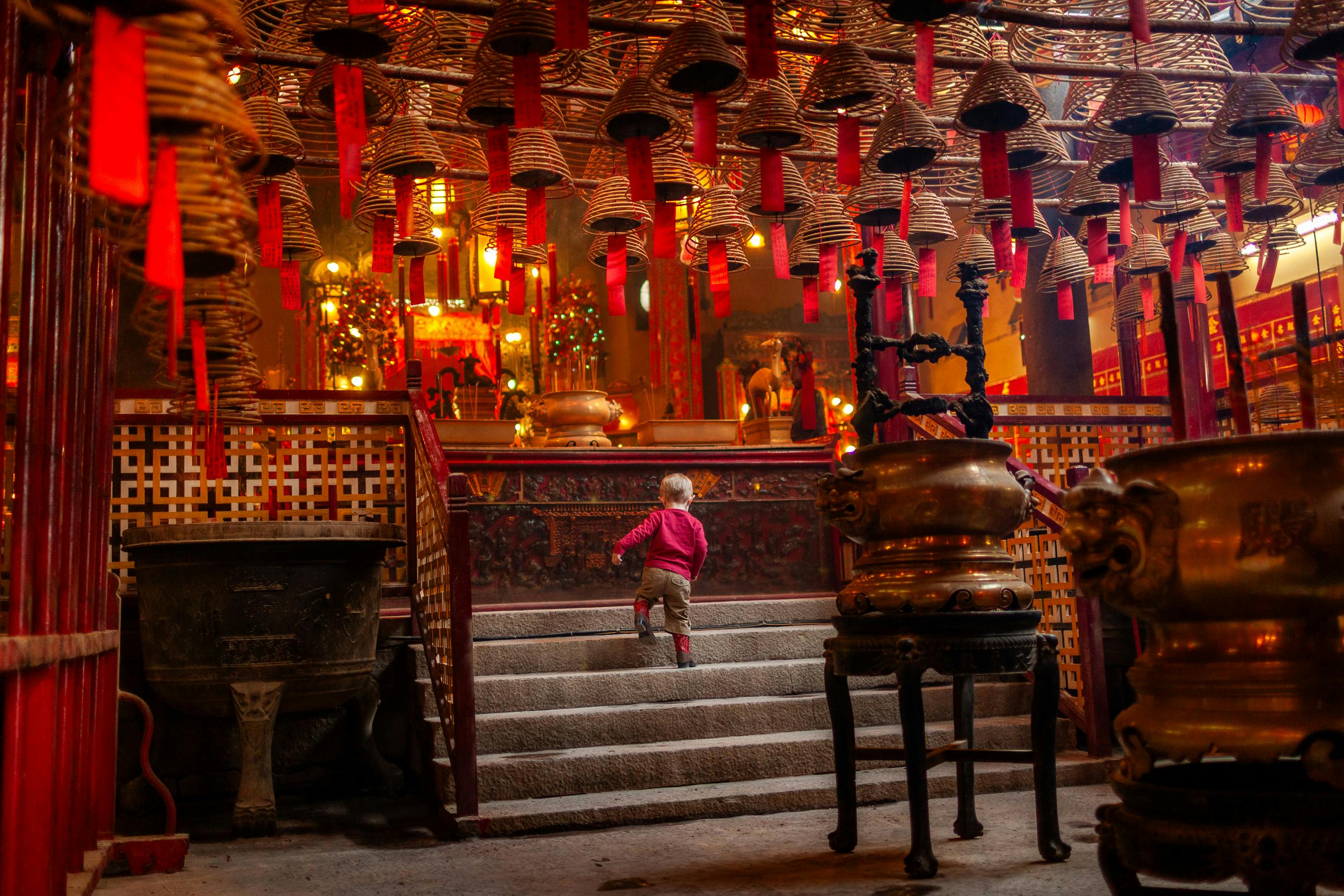 A young child climbs steps inside the ornate Man Mo Temple in Hong Kong, showcasing traditional culture and atmosphere.