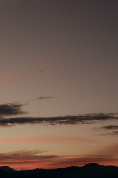 Free Tranquil twilight sky with mountains silhouetted against soft sunset hues and a distant airplane. Stock Photo