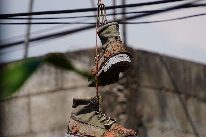 A pair of vintage, worn-out boots hanging on a wire against a concrete wall, showcasing street art vibe.