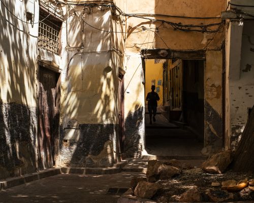 Free A runner's silhouette in a sunlit and shadowed alley, creating a dramatic urban scene. Stock Photo