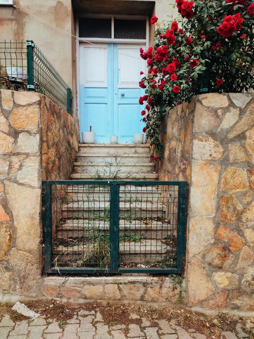 Free Rustic stone steps leading to a blue door, adorned with vibrant red flowers in Sinop, Türkiye. Stock Photo