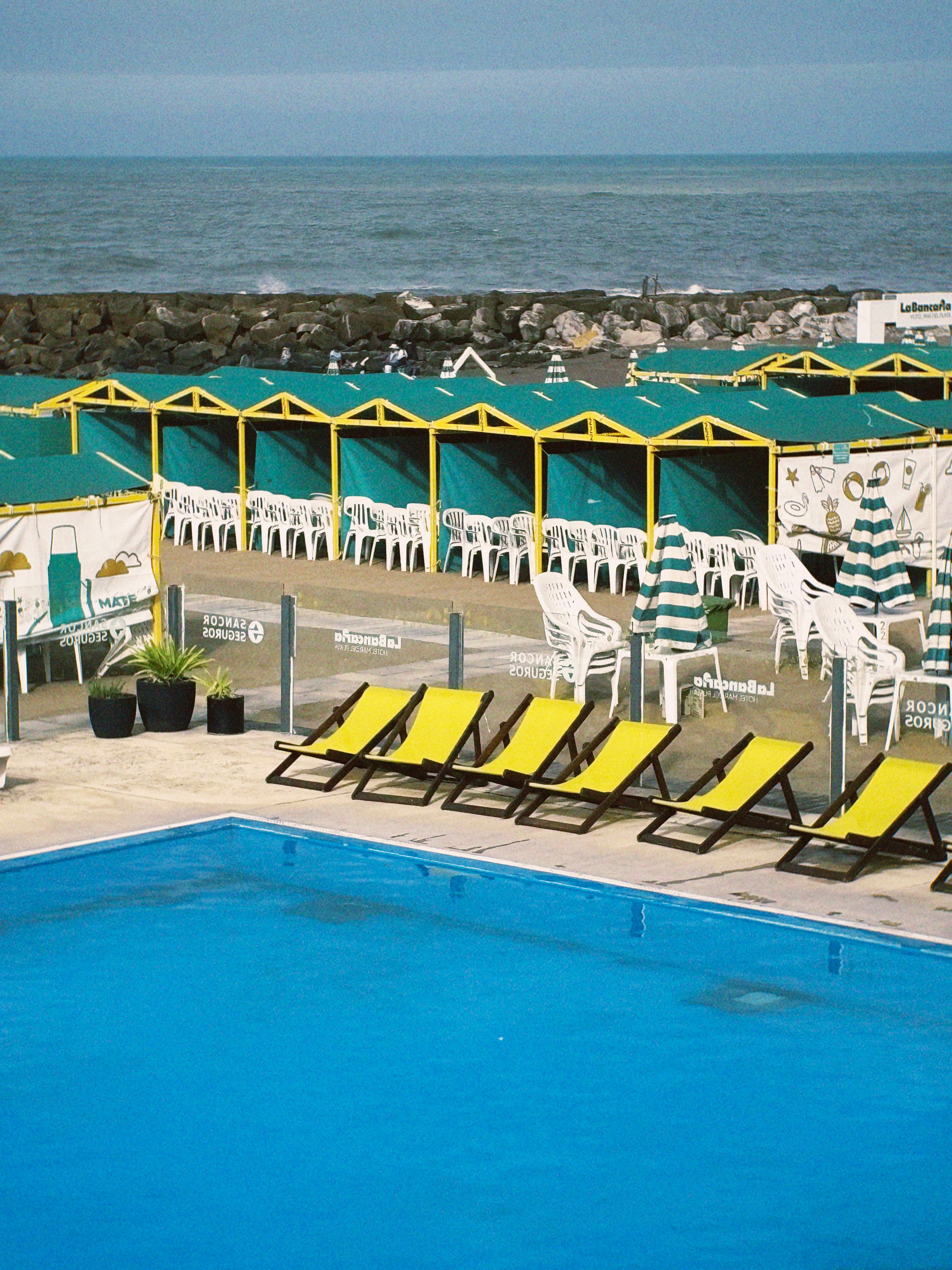 Lively beachside scene featuring a pool, yellow loungers, striped umbrellas, and ocean view.