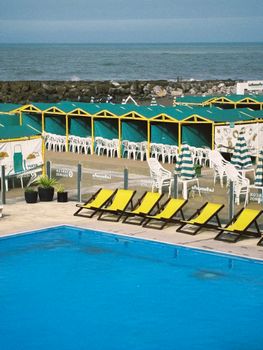 Lively beachside scene featuring a pool, yellow loungers, striped umbrellas, and ocean view.