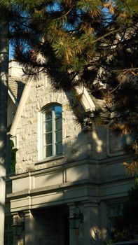 Sunlit stone house façade with architectural details and pine tree shadows.