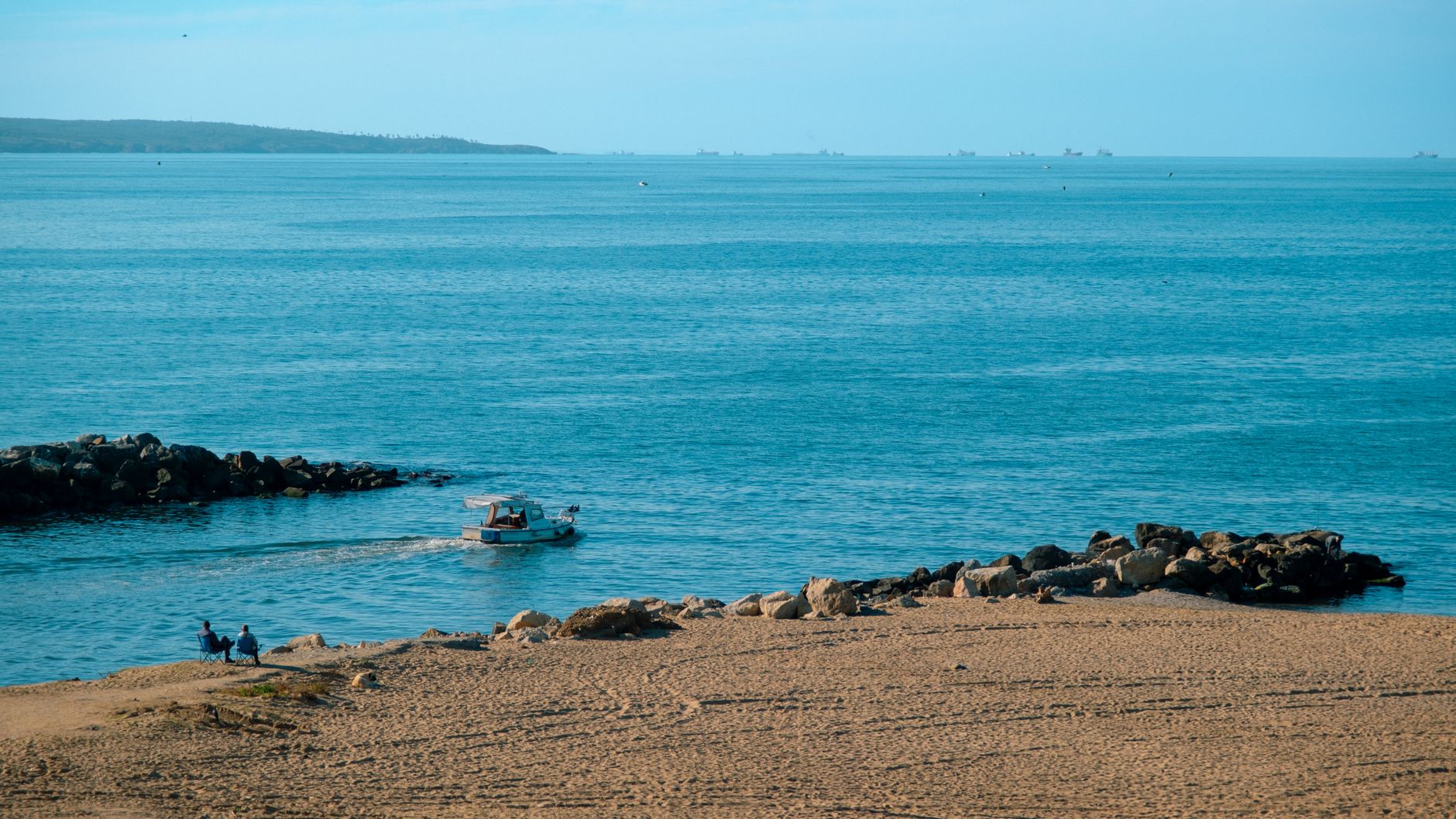 Tranquil beach scene in Riva, Istanbul with a boat on the water and rocky shores.