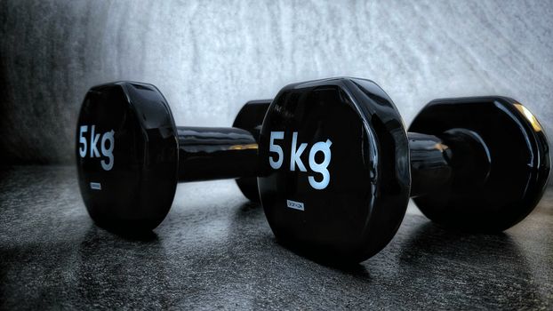Close-up of two 5kg dumbbells on a textured dark background, showcasing fitness equipment.