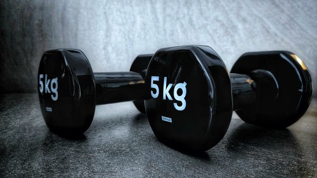 Set of black 5kg dumbbells placed on a textured surface with a dark tone.