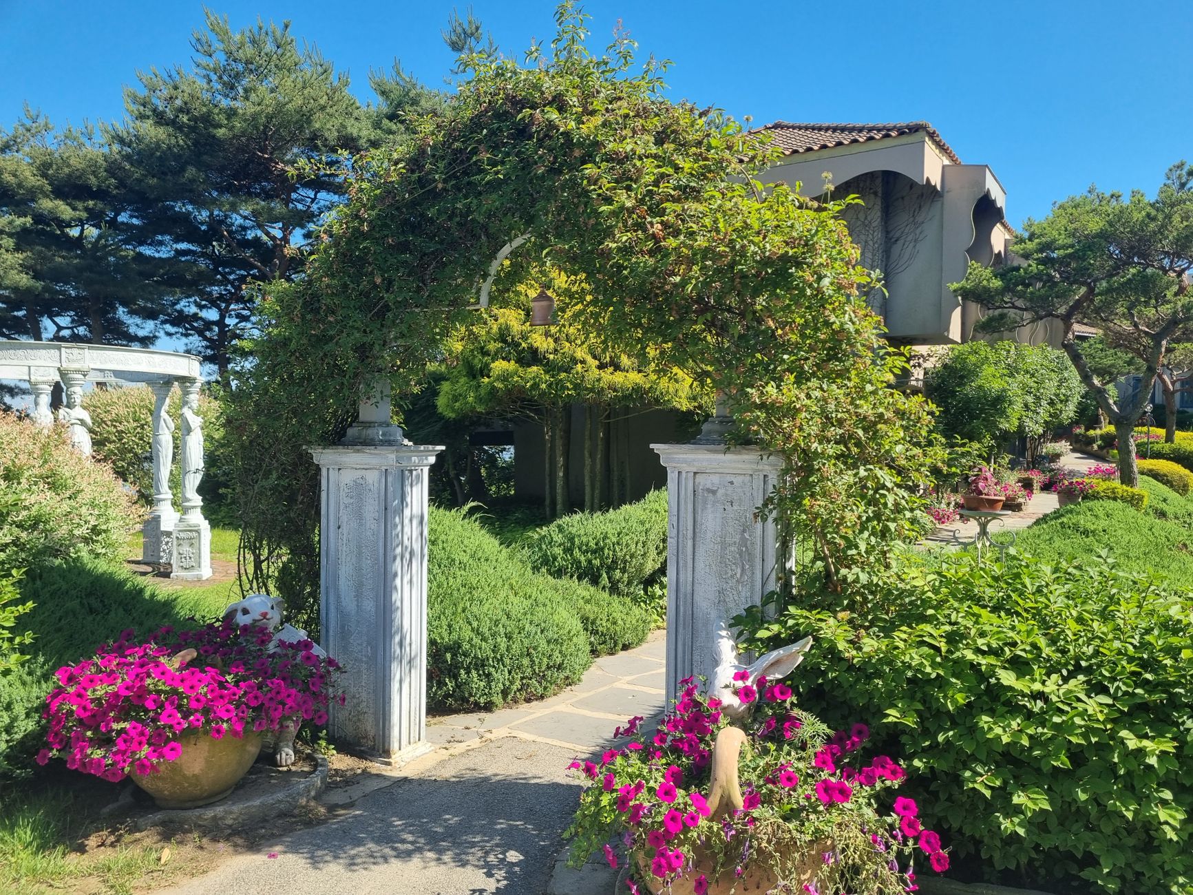 A vibrant garden scene with an arched entrance framed by flowers and stone sculptures.