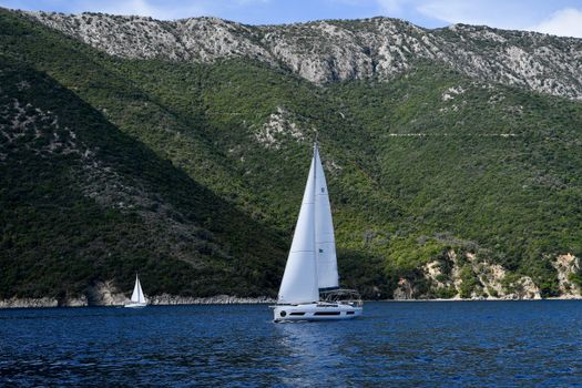 Sailboats gliding along the picturesque Ionian Sea, framed by lush green cliffs on a clear summer day.