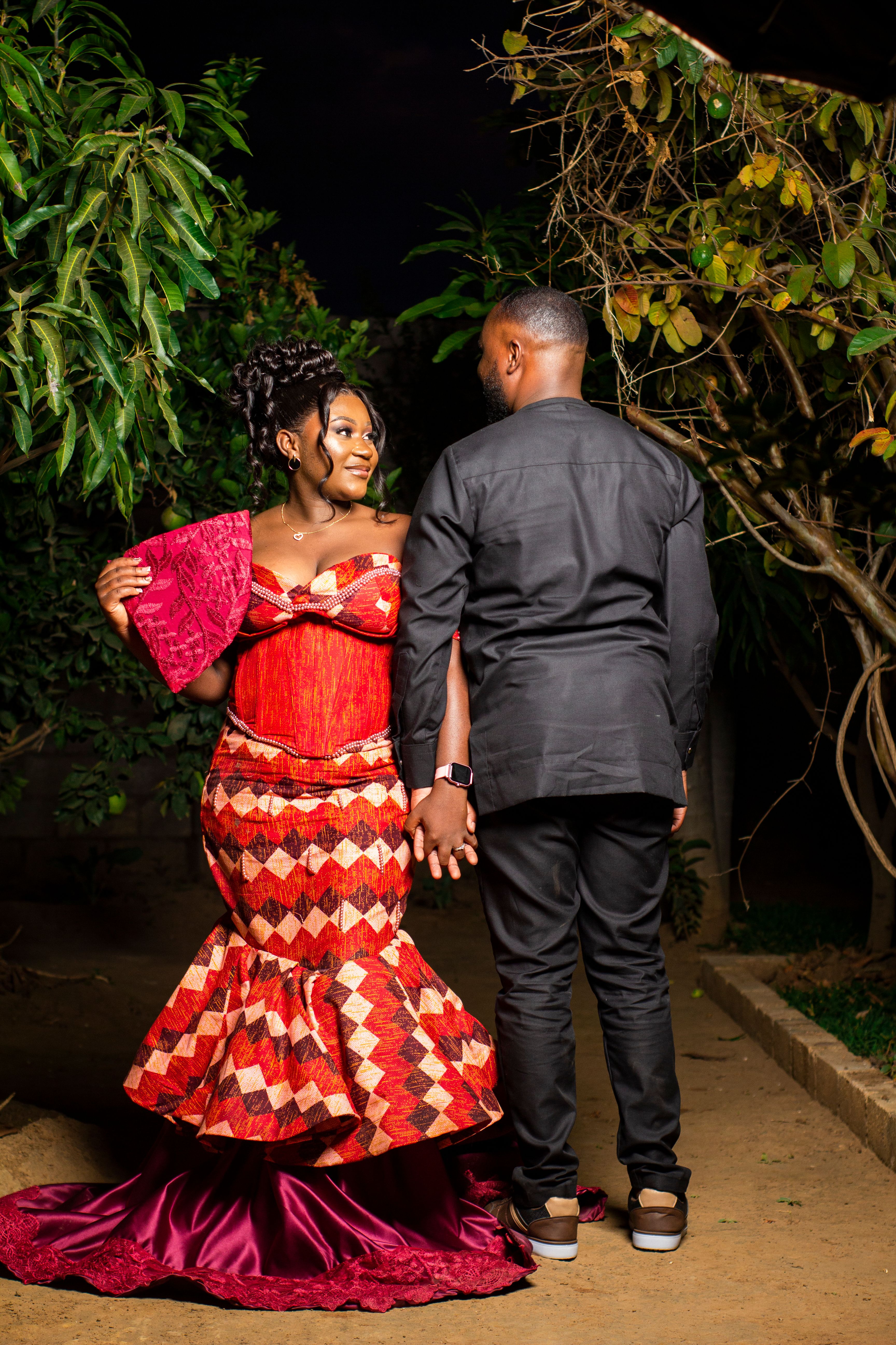 A stylish couple in vibrant traditional African attire poses outdoors, exuding elegance and joy.