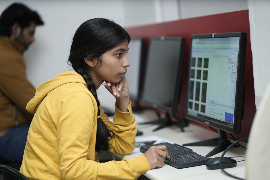 Woman in yellow hoodie focused on computer work, indoor office.