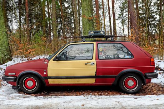 A classic two-tone car with stickers parked in a snowy winter forest setting.