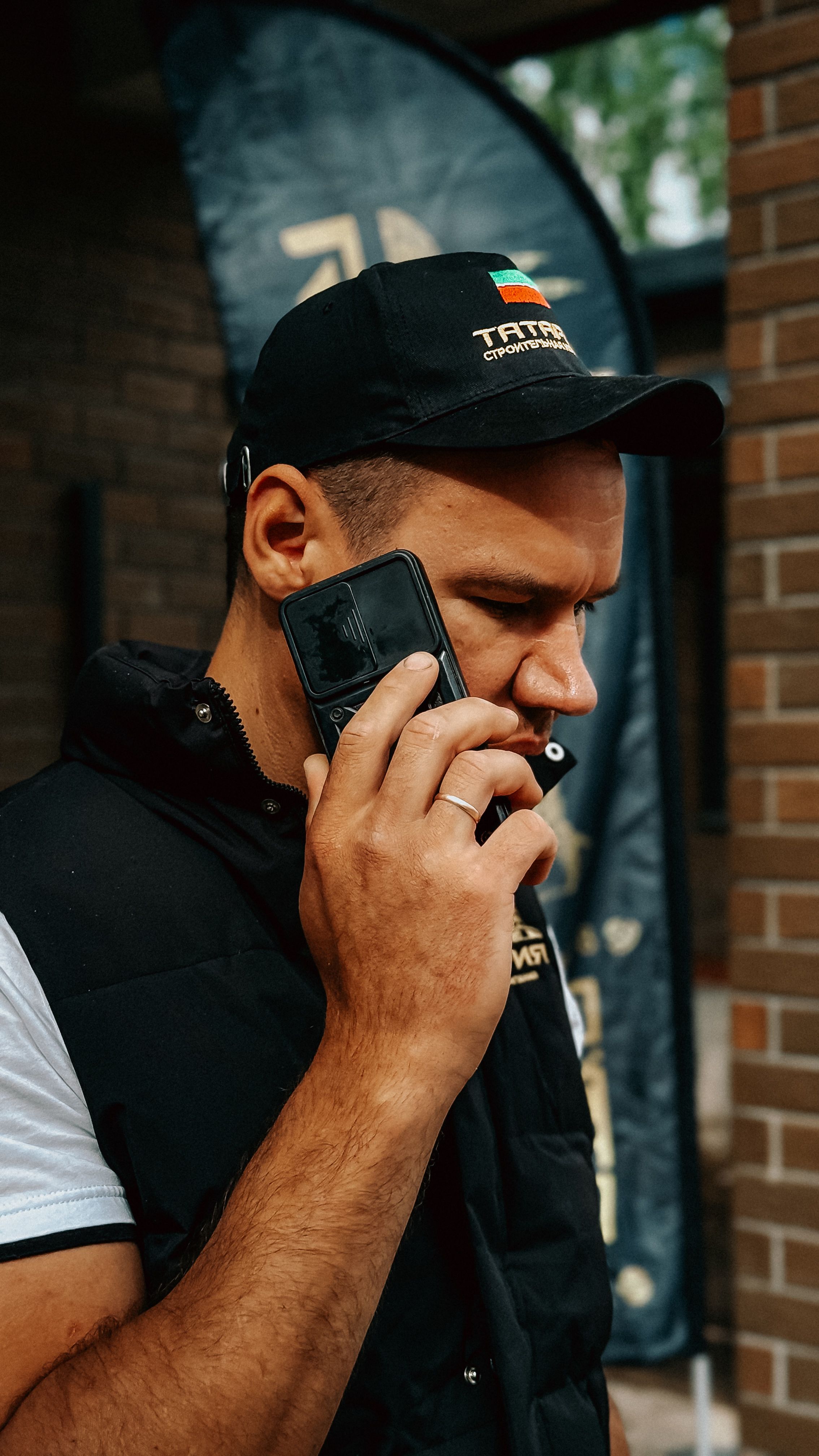 A man in casual clothing and cap talking on a smartphone outside with a focused expression.