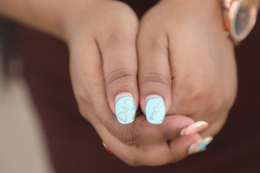 Detailed shot of hands featuring light blue nails with 'Mom' and 'Dad' written, showcasing personalized nail art.