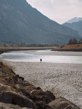 A lone individual stands by a serene river surrounded by Swiss Alps.