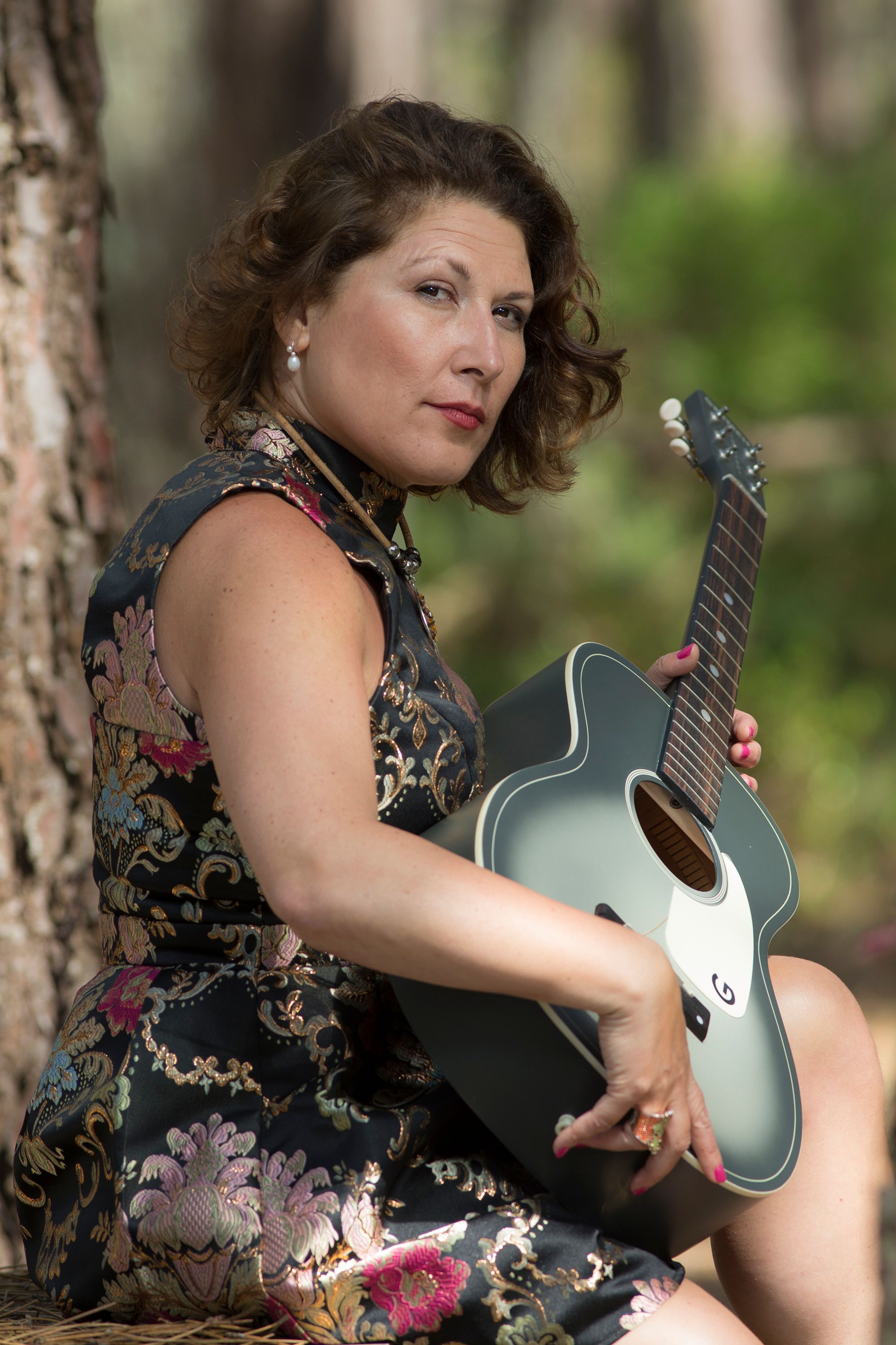 A woman enjoys playing an acoustic guitar amidst a serene forest setting.