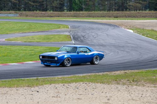 Free A vibrant blue vintage car skillfully drifting on a winding racetrack under a clear sky. Stock Photo