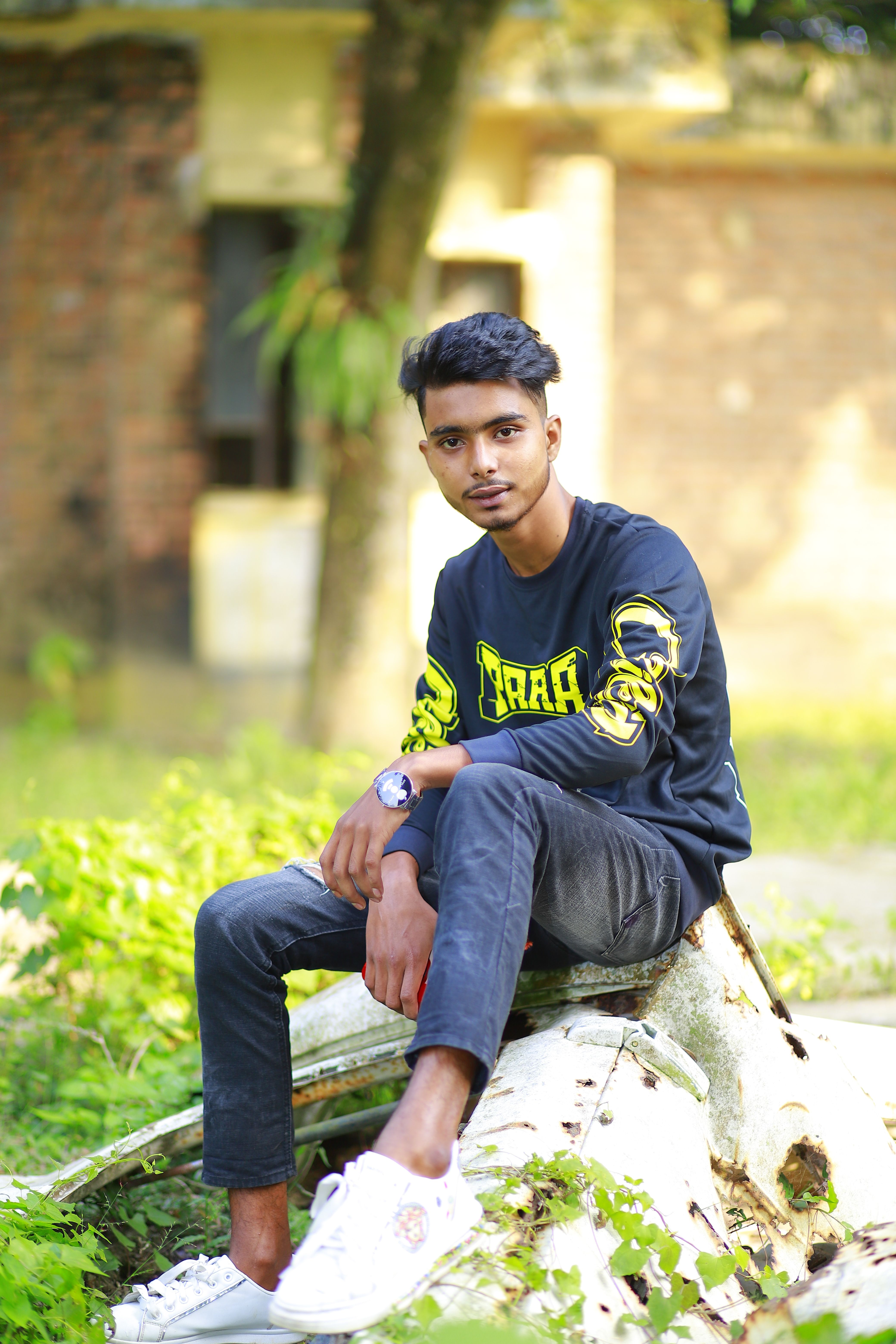 Portrait of a young man sitting on a tree trunk outdoors in Brahmanbaria, Bangladesh.