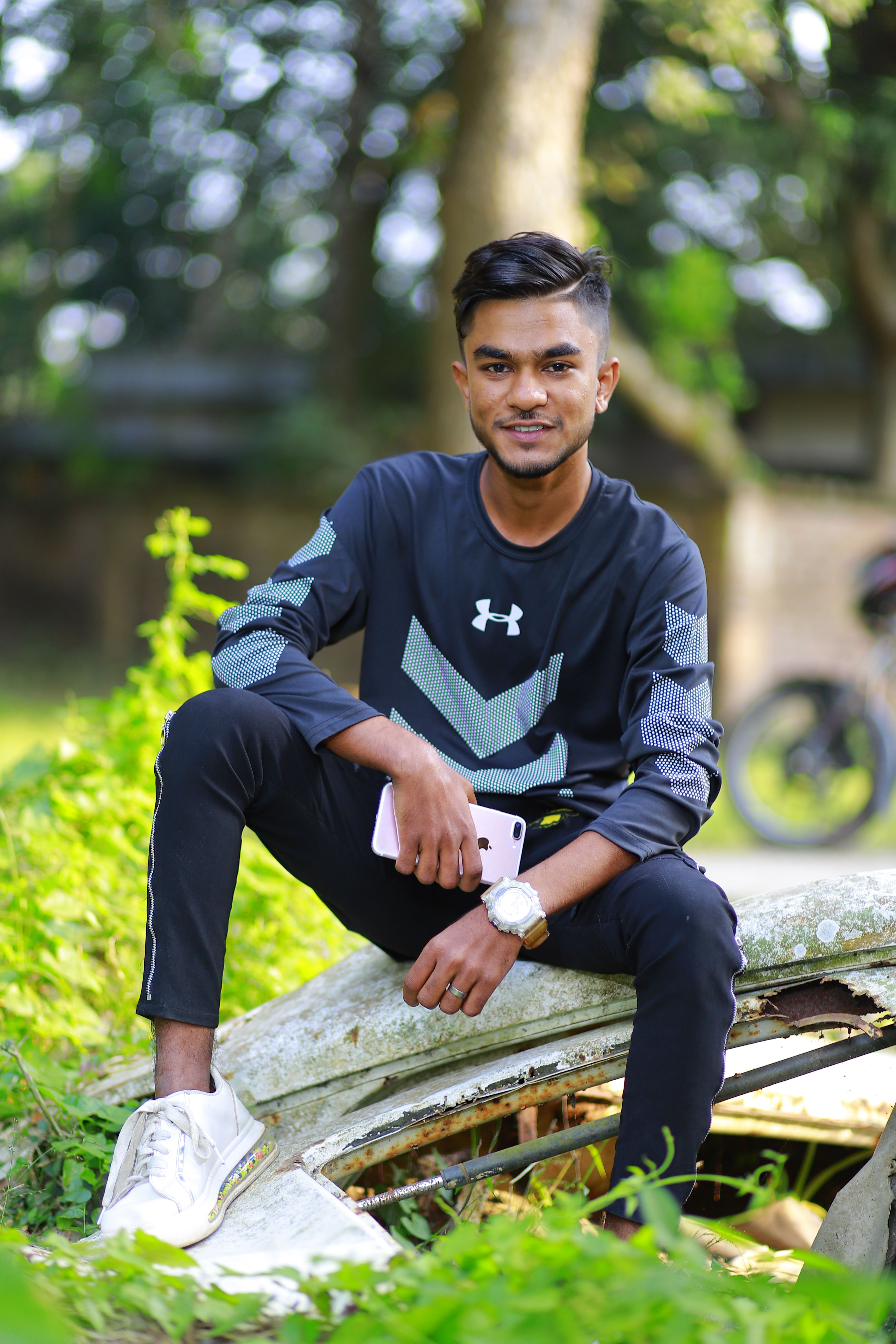 Young man in casual clothing posing outdoors in lush green surroundings, showcasing style and confidence.