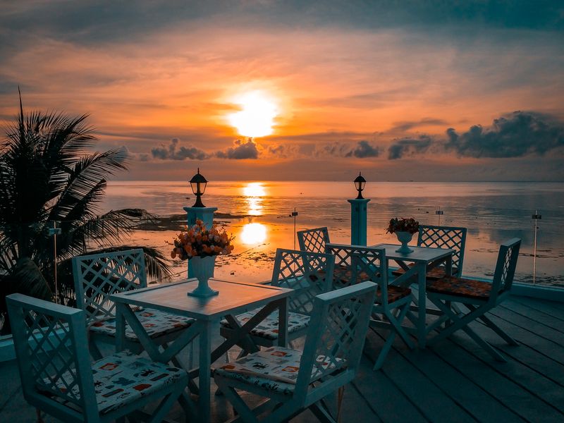 Outdoor dining setup with white tables and chairs overlooking the ocean at sunset