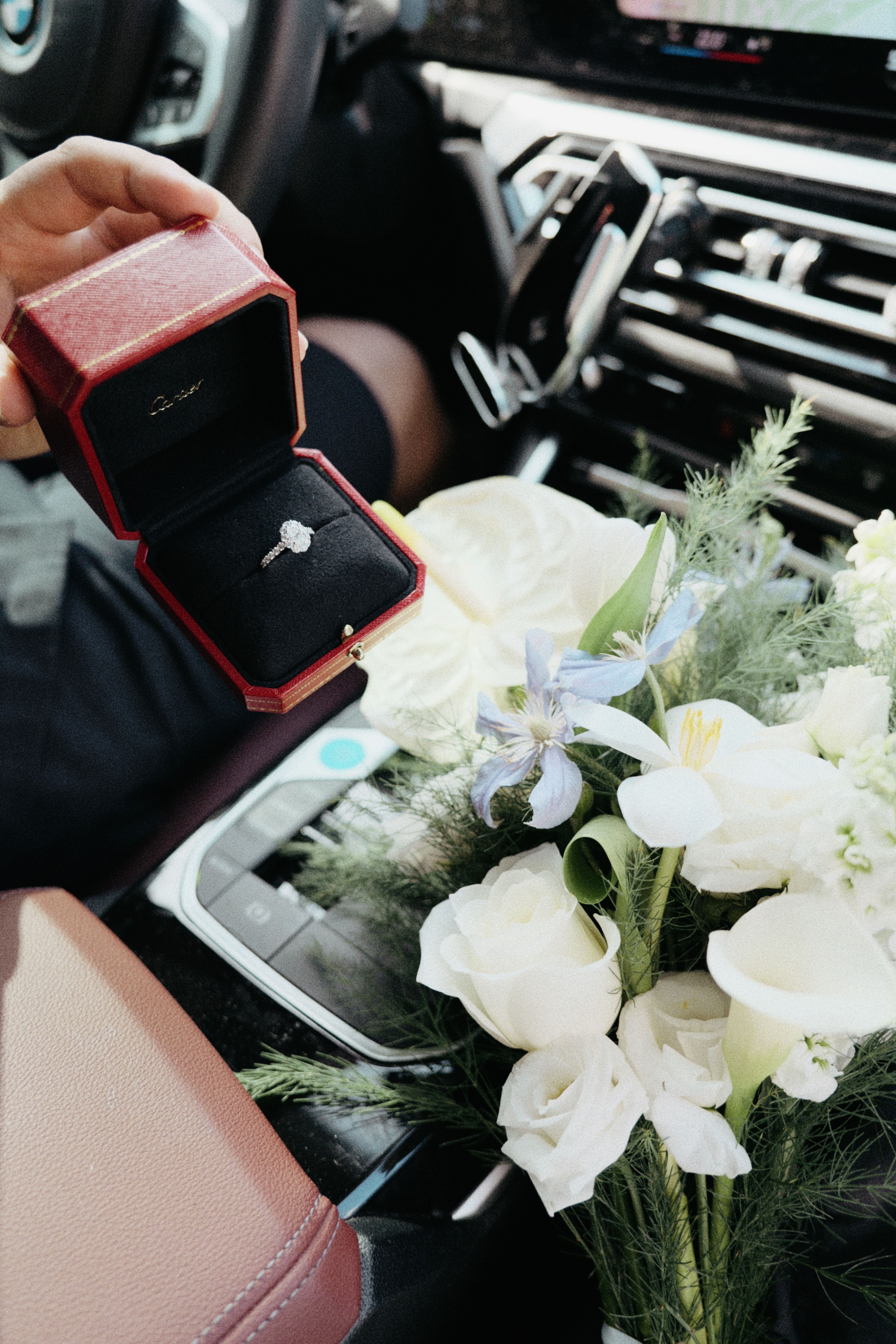 Engagement ring in box with bridal bouquet inside car, symbolizing wedding planning and romance.