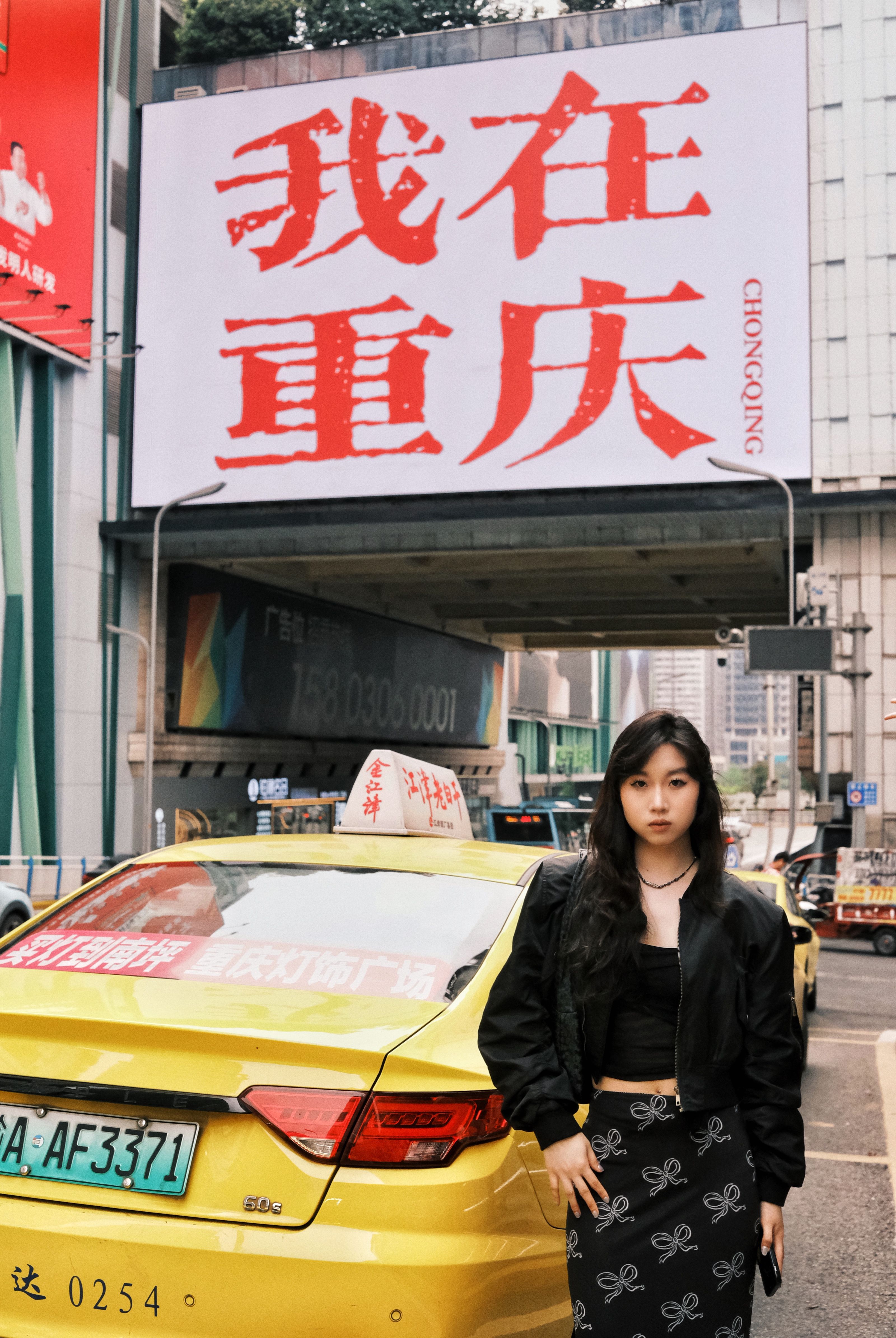 Urban street scene in Chongqing featuring a woman beside a yellow taxi under a large sign.