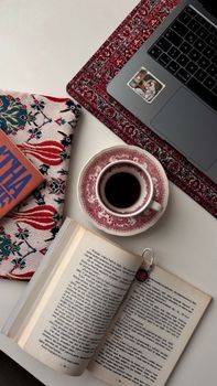Top view of a laptop, coffee, and open book on a decorated desk, creating a cozy work environment.