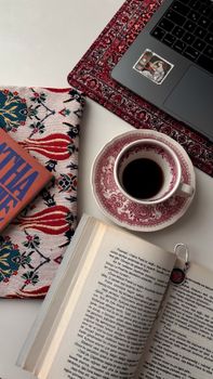 Overhead view of a cozy setting with a book, coffee, and laptop on a patterned surface.