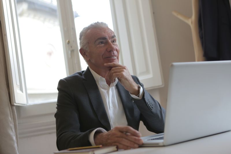 Elderly businessman in black suit smiling while working on laptop