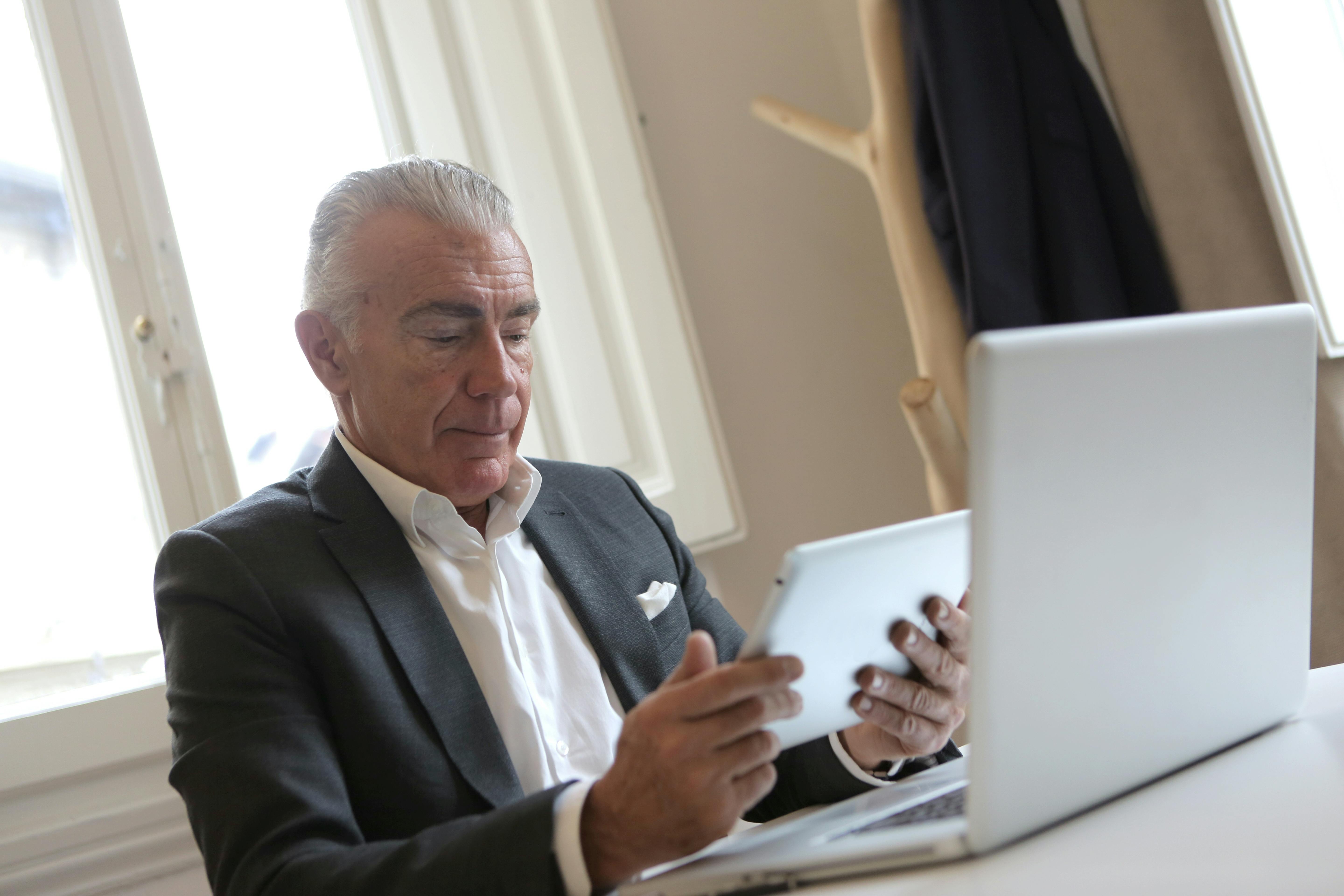 Senior businessman in office attire working on a tablet and laptop.