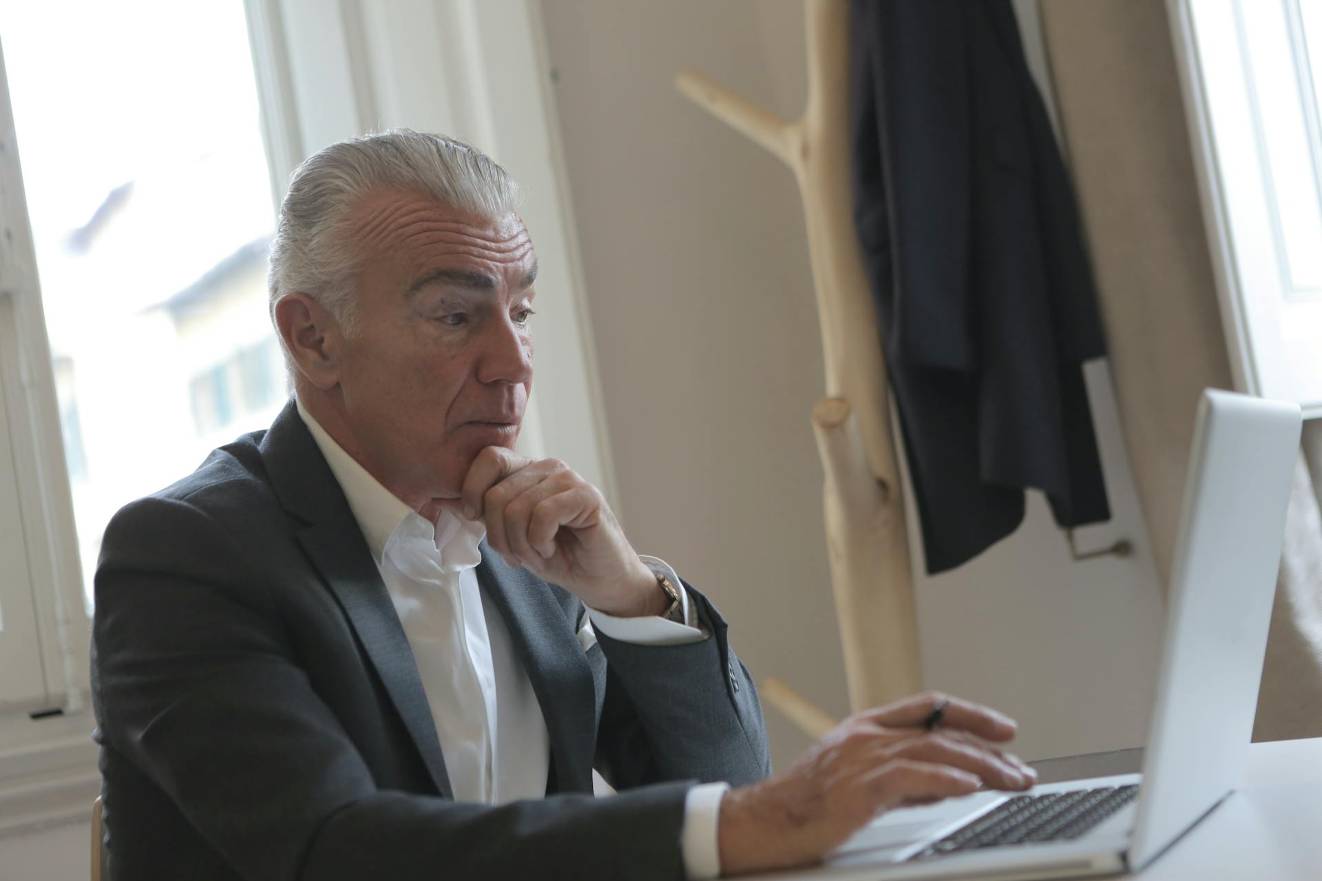 An elderly businessman concentrating while working on a laptop at his office desk.