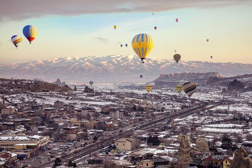 Free Aerial view of hot air balloons over a snowy Cappadocia, Turkey, with mountains in the background. Stock Photo