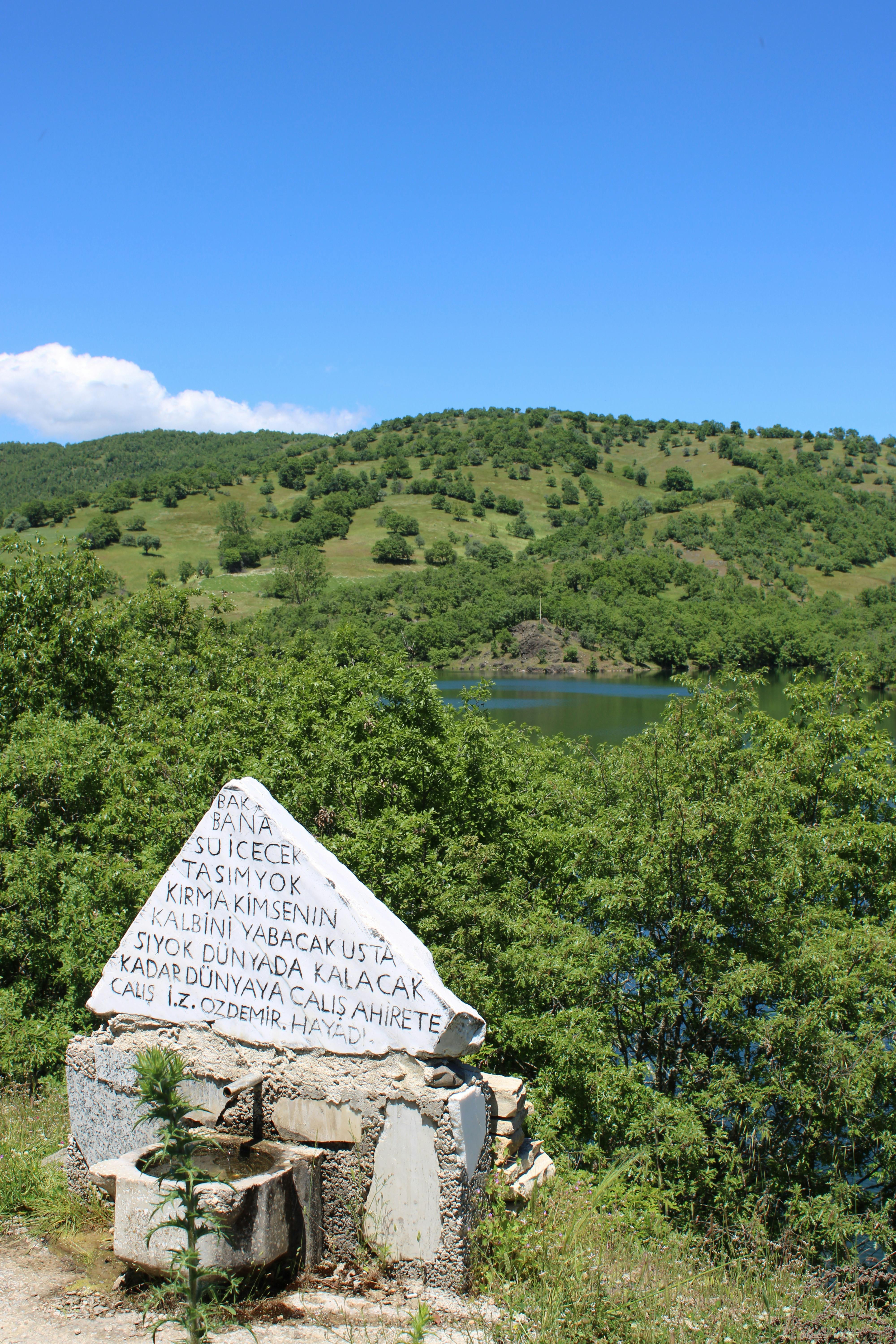Stone monument with inscription against lush greenery and blue sky.