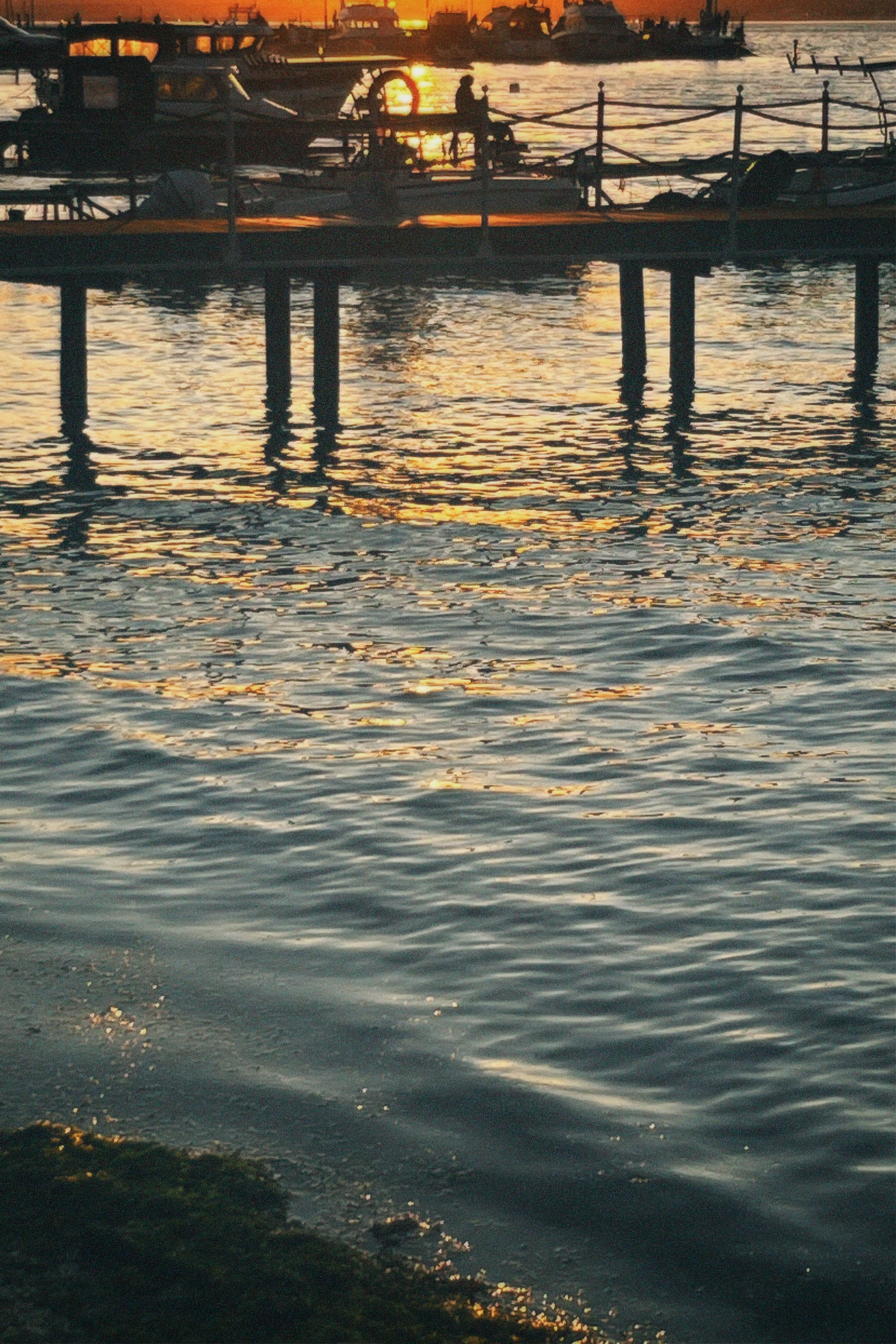 Sunset over a peaceful pier with boats and gentle waves reflecting golden hues.