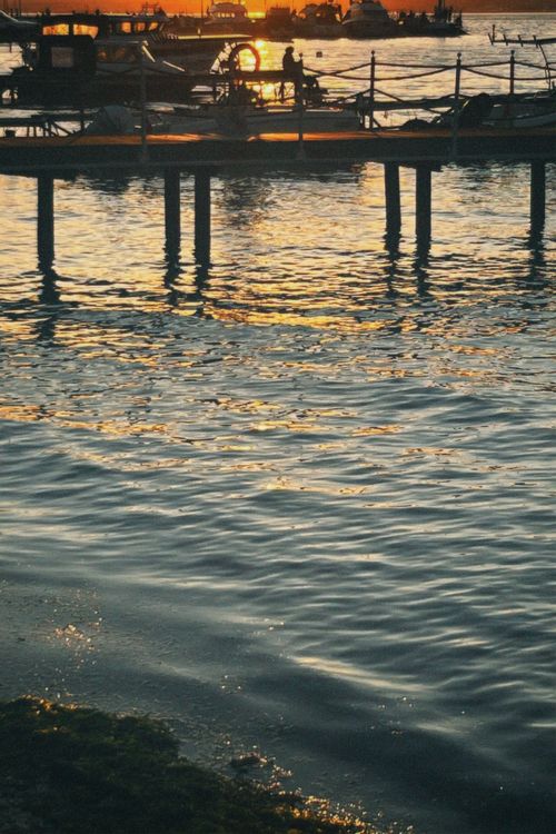 Free Sunset over a peaceful pier with boats and gentle waves reflecting golden hues. Stock Photo