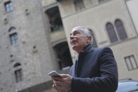 From below of mature gentleman in classy wear standing near building in city and checking message on cellphone while looking up