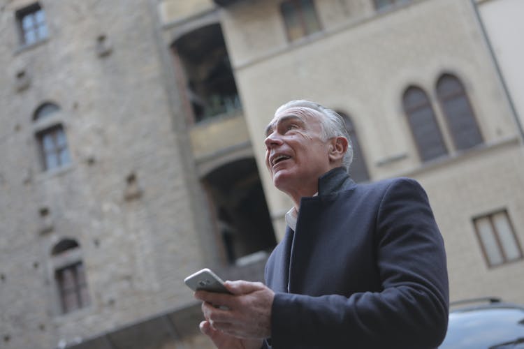 Elegant Senior Man Browsing Smartphone On City Street