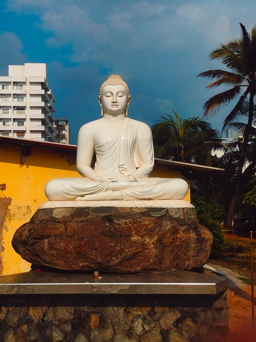 Free A tranquil Buddha statue sits majestically on a stone base amidst a city backdrop. Stock Photo