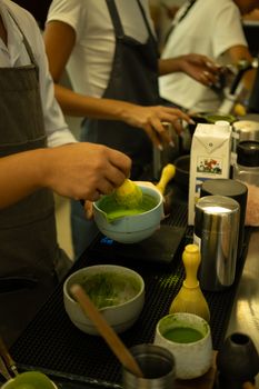 A barista skillfully prepares matcha tea using a bamboo whisk in a cafe setting.