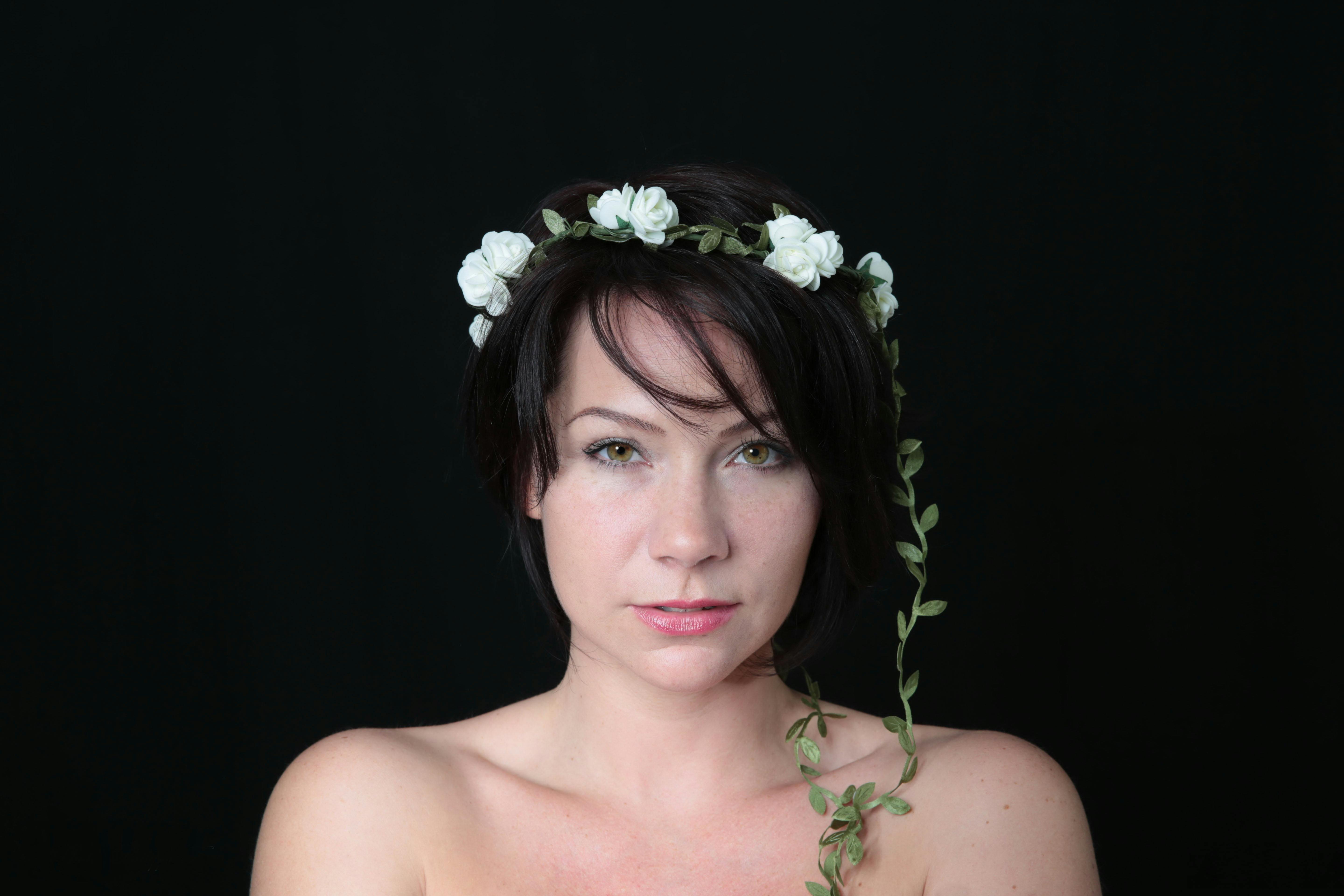 Elegant portrait of a woman wearing a floral wreath, set against a black background.