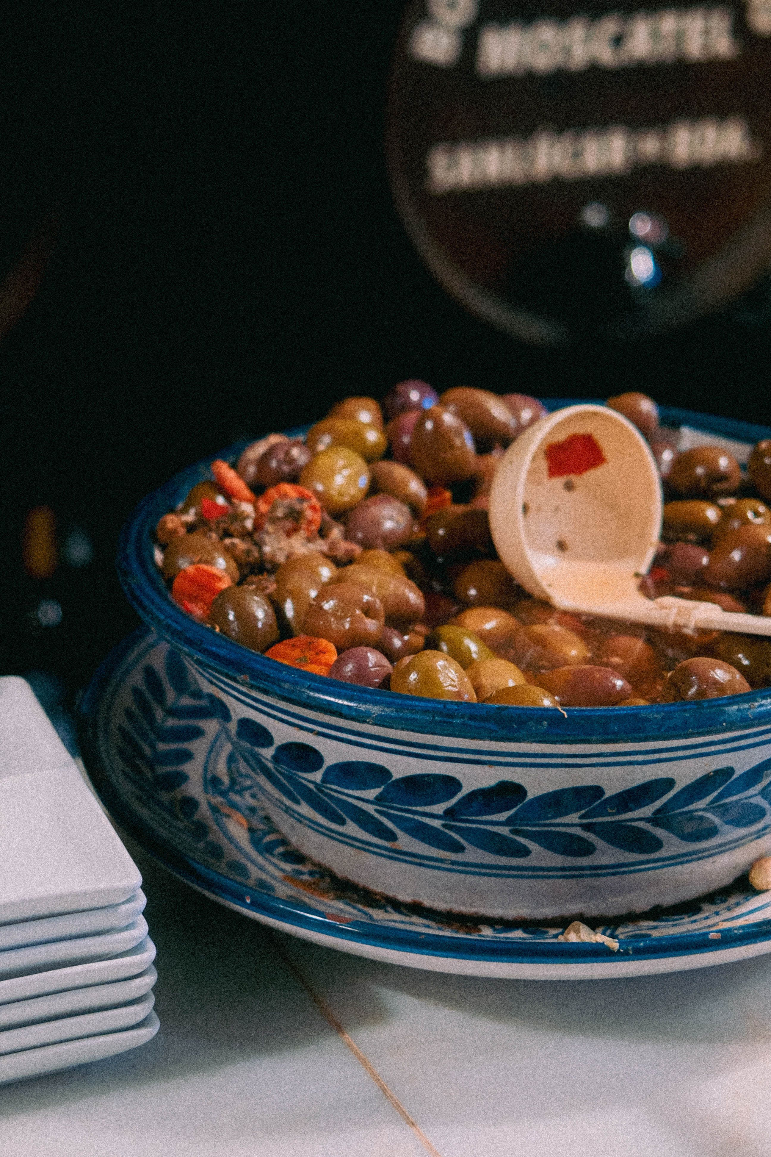 Grand bol en céramique bleue et blanche rempli d'olives marinées aux piments, avec sa cuillère en bois