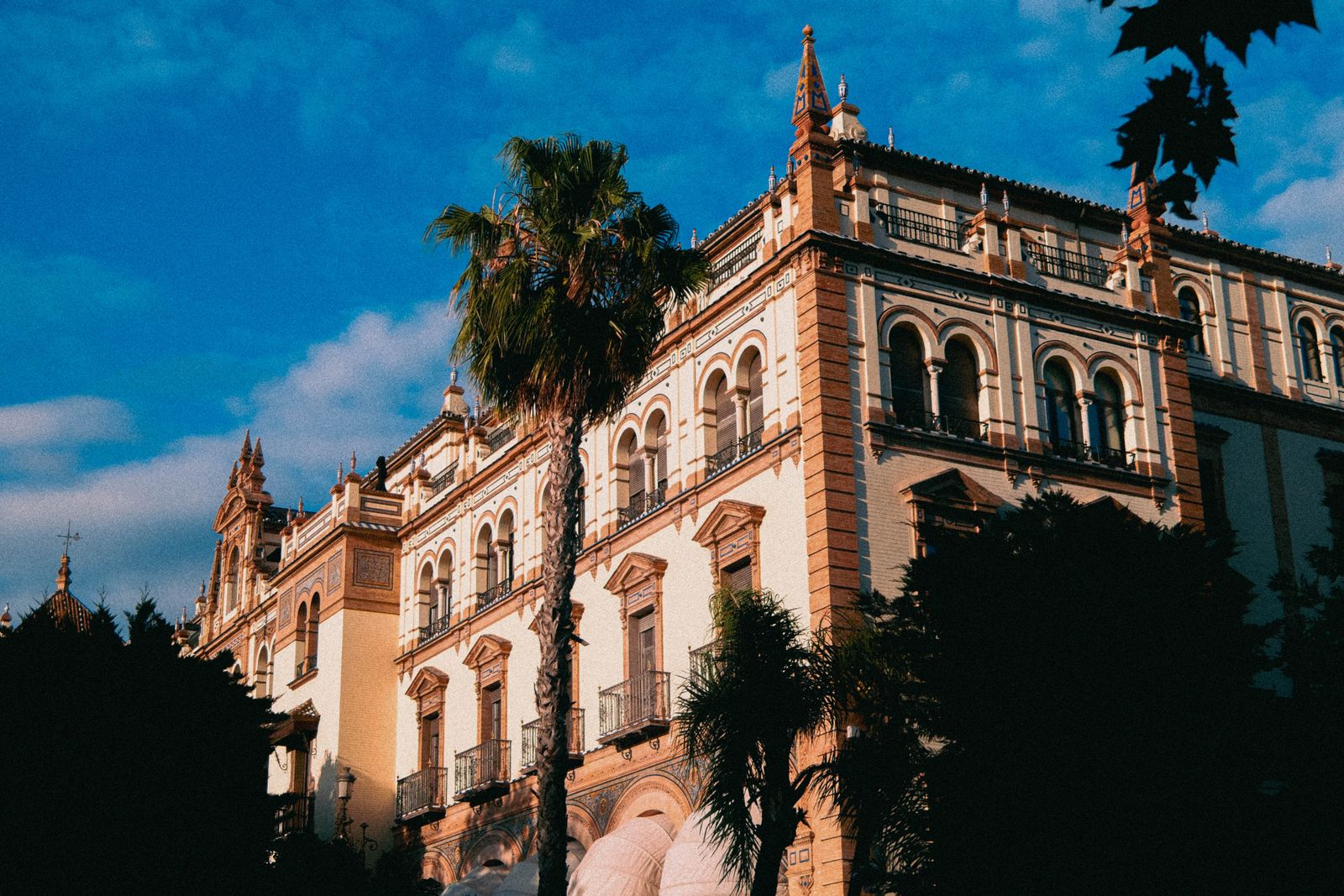 Ornate Spanish-style hotel facade with palm tree in warm sunlight, Seville
