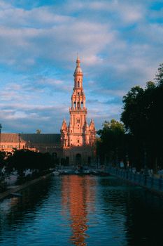 Beautiful view of Plaza de España in Seville reflecting in water at sunset.