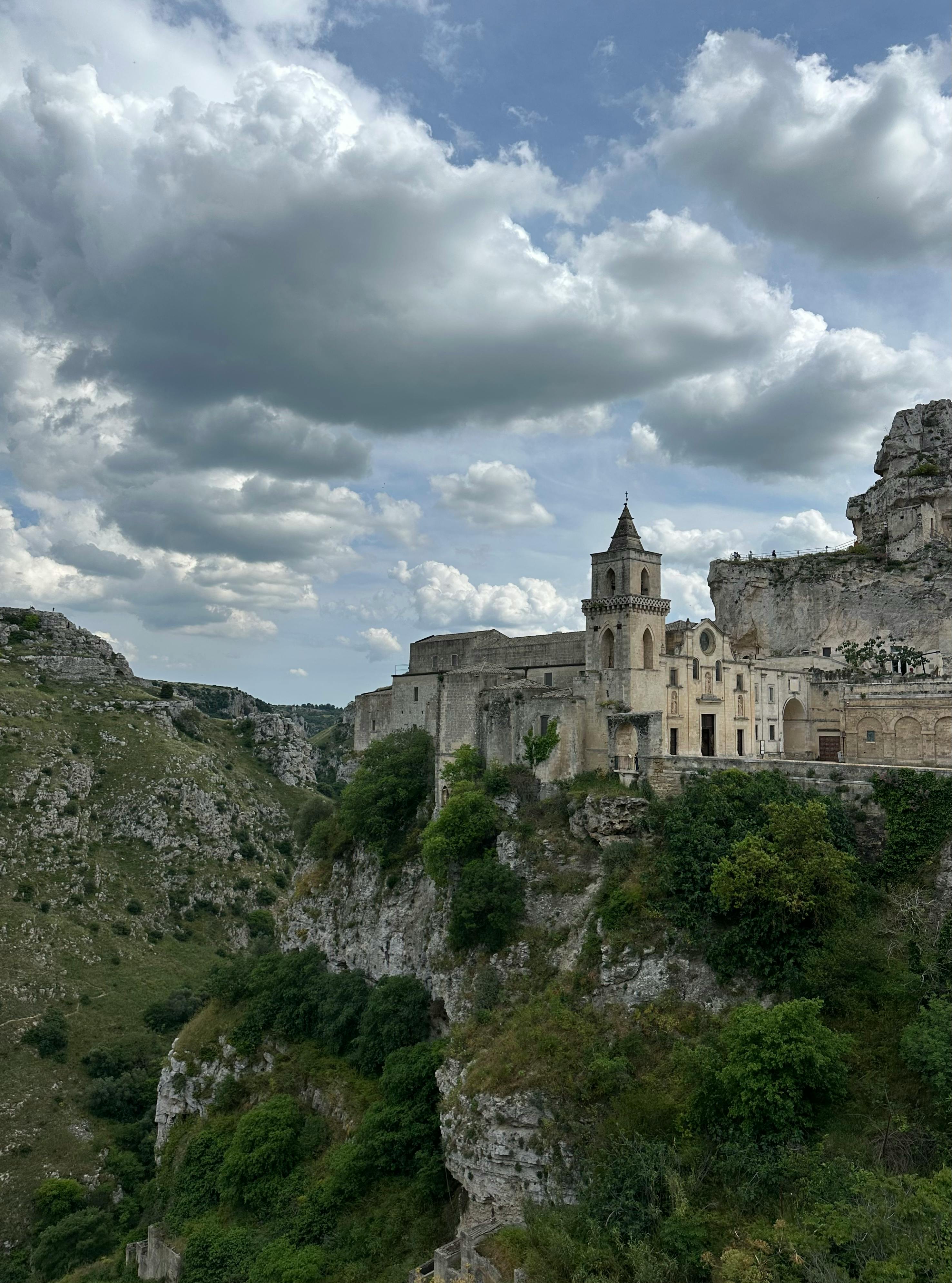 Explore the stunning cliffside architecture of Matera, Italy with this historic church view against a dramatic sky.