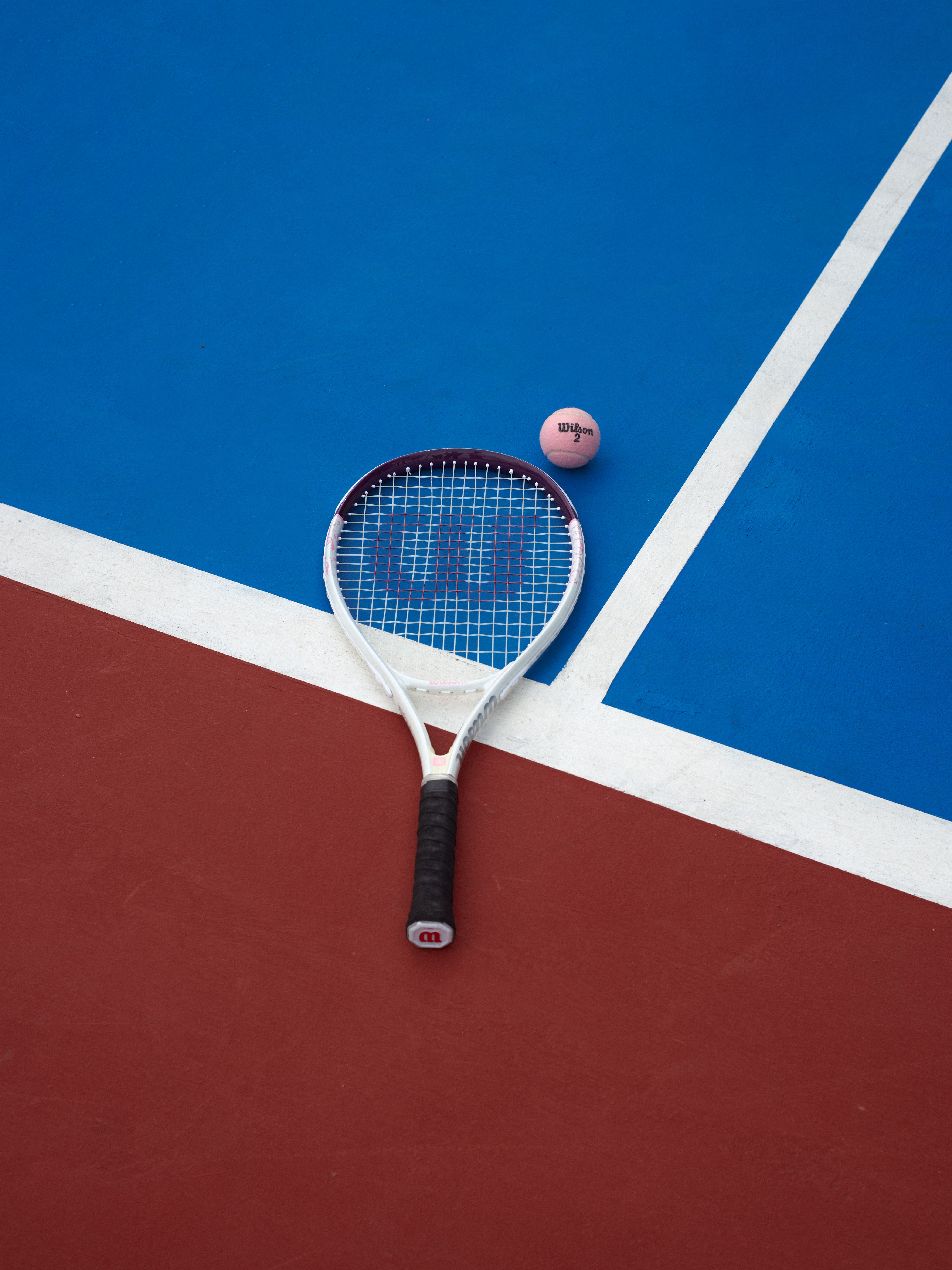Tennis racket and ball on a vibrant red and blue court surface.