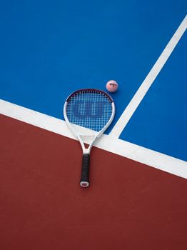Tennis racket and ball on a vibrant red and blue court surface.