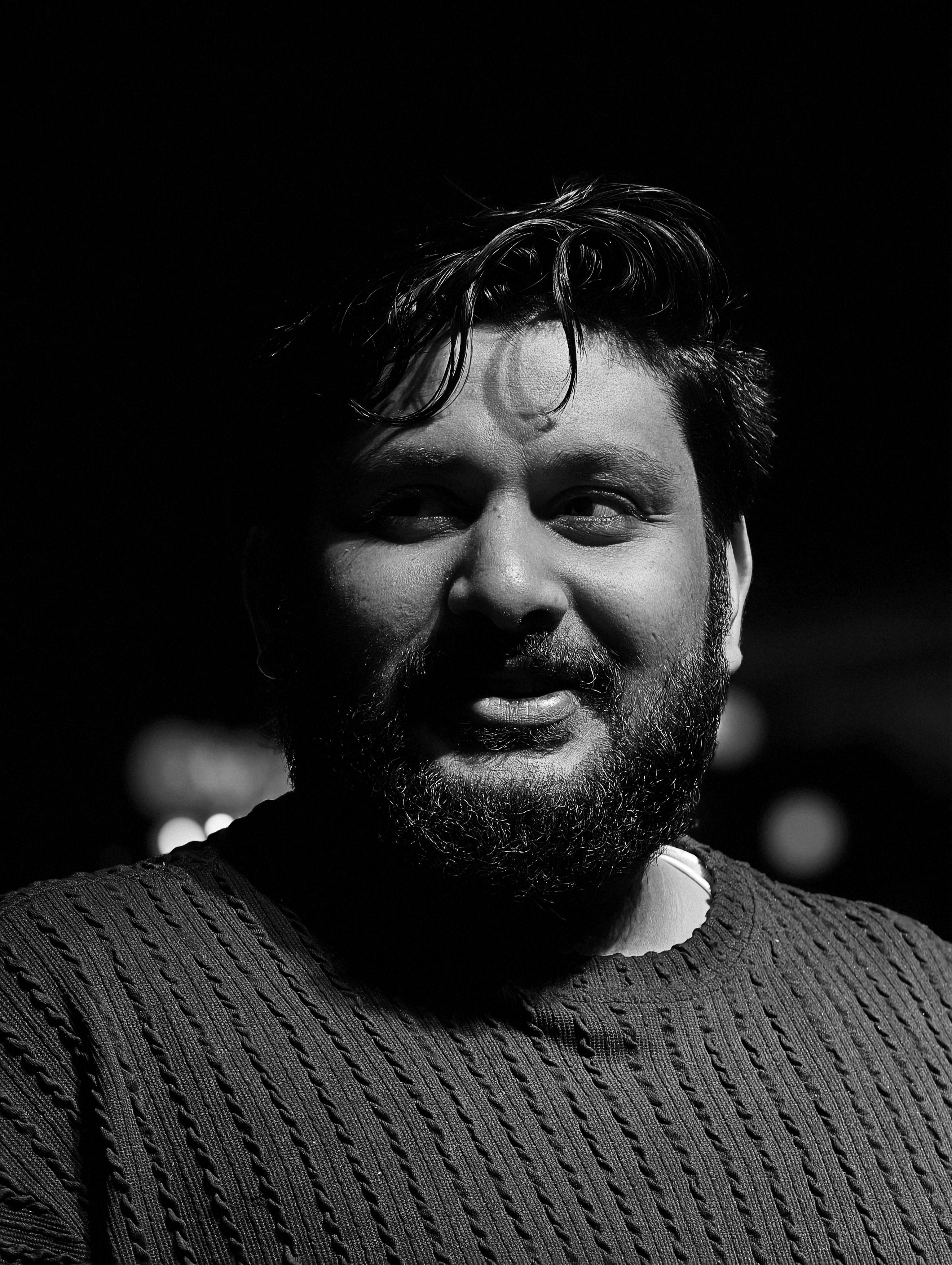 A striking black and white portrait of a bearded man in a textured sweater, captured with high contrast lighting.