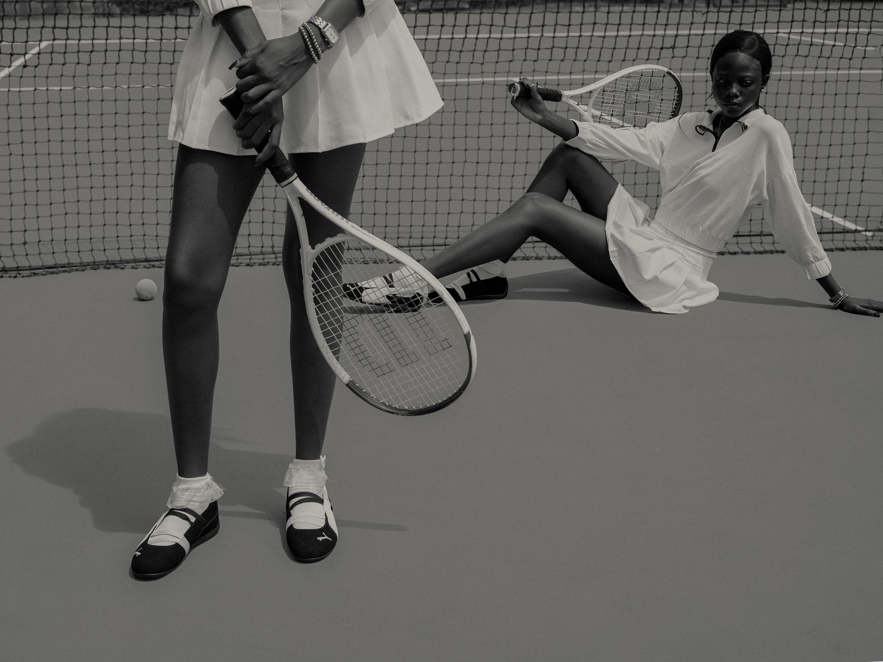 Stylish black and white image of two women on a tennis court, showcasing fashion and sports.